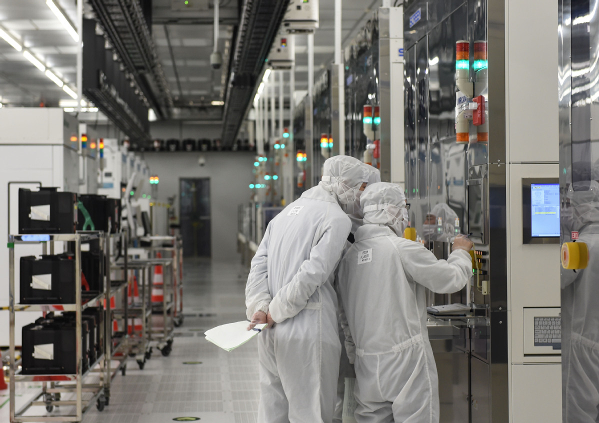 Engineers in white cleanroom suits operating equipment inside an SMIC chip fabrication plant.