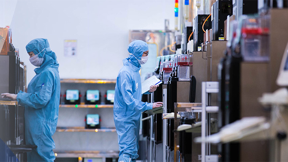 Workers in blue cleanroom suits inspecting equipment along a semiconductor production line.
