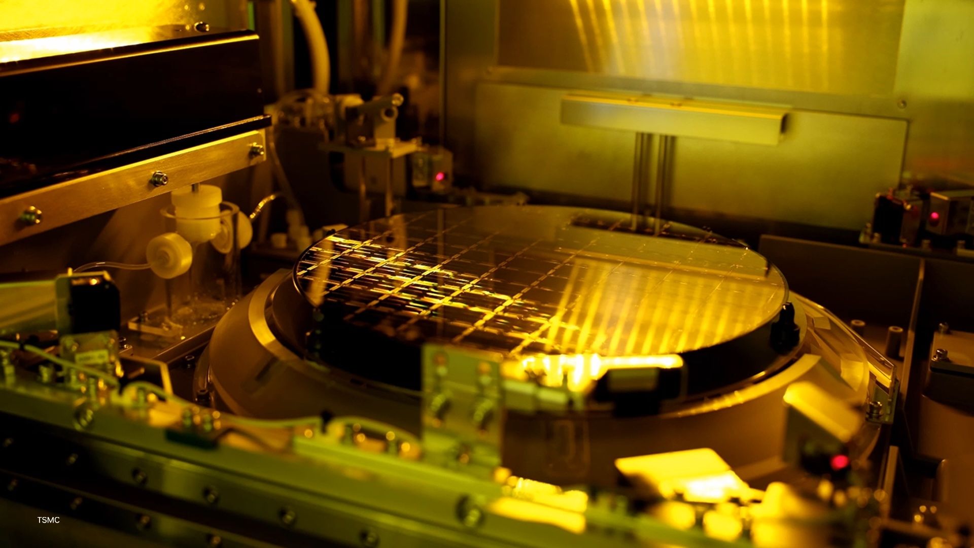 A silicon wafer covered in chip dies glowing under golden lithography light inside a TSMC fab.